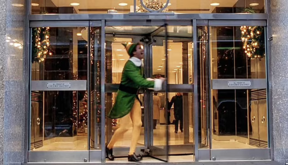 Screenshot from the movie Elf. Buddy playing with a revolving door.